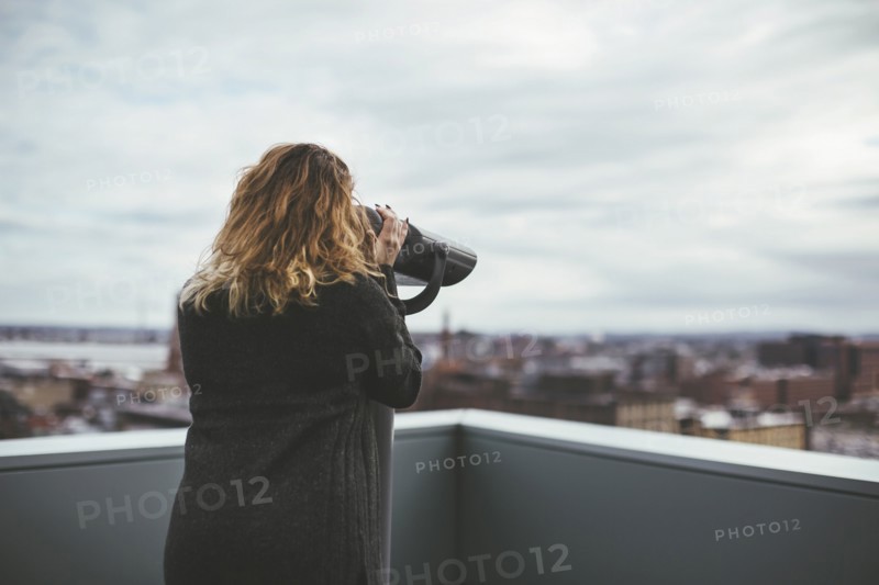 Caucasian woman on urban rooftop admiring cityscape with telescope