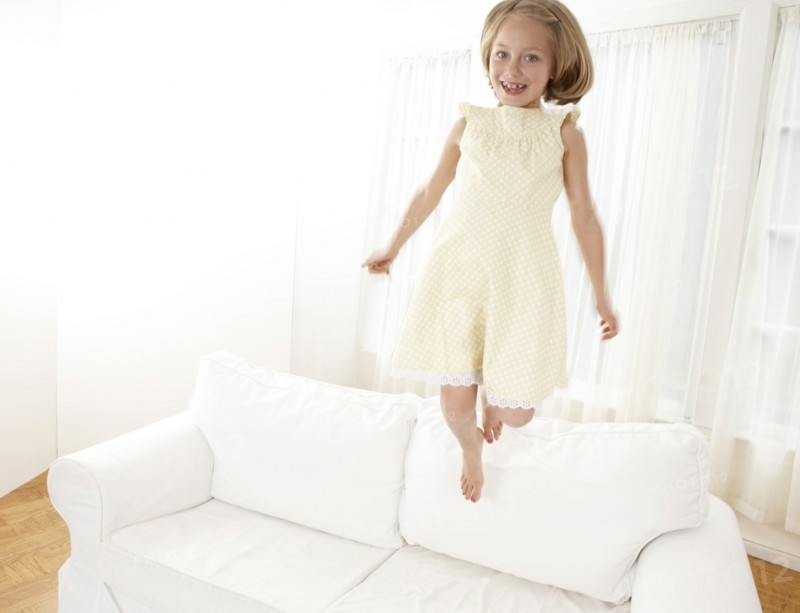 Caucasian girl jumping on sofa in living room