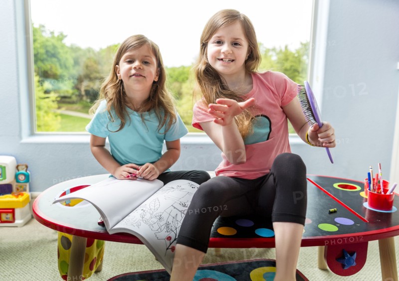 Caucasian sisters drawing at table in playroom