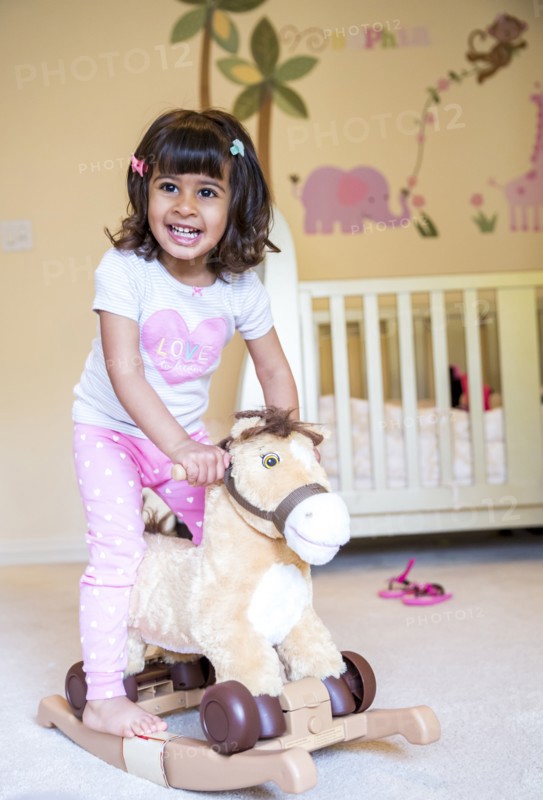 Girl riding rocking horse in nursery