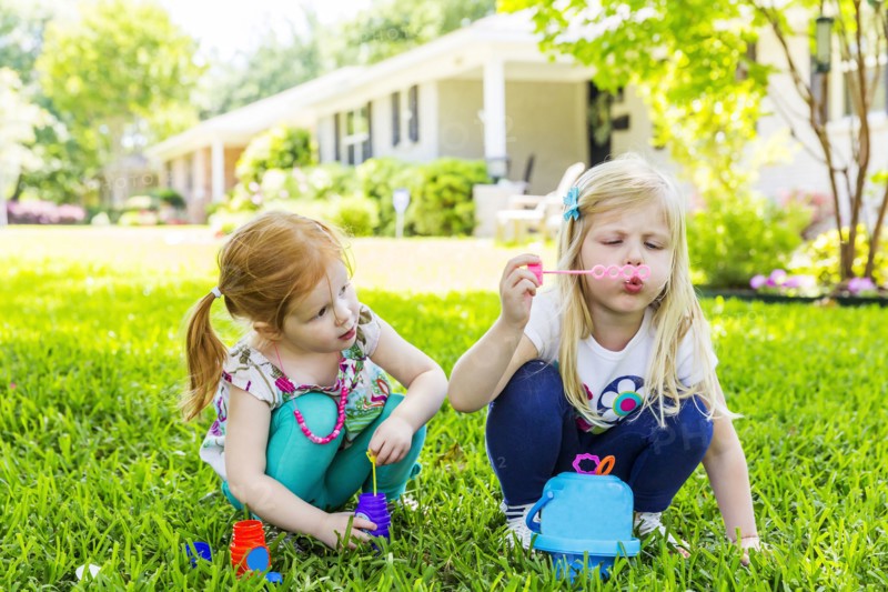 Caucasian sisters blowing bubbles in backyard