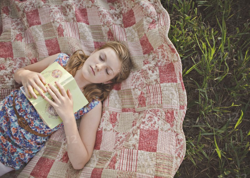 Caucasian girl sleeping with book on blanket