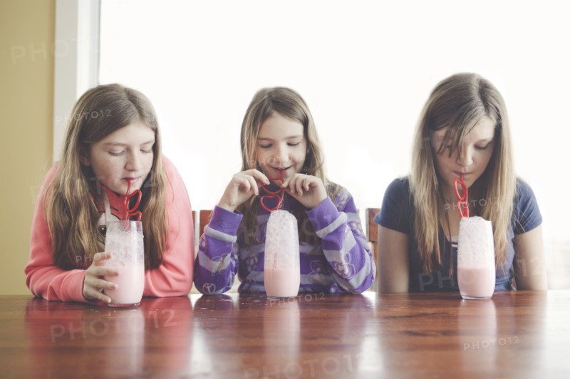 Caucasian girls drinking milk with curled straws at table