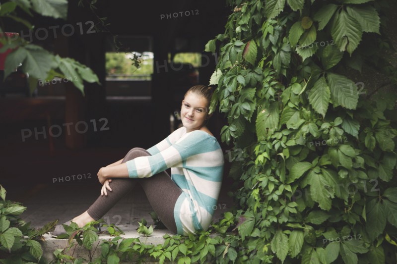 Caucasian teenage girl sitting at ivy wall