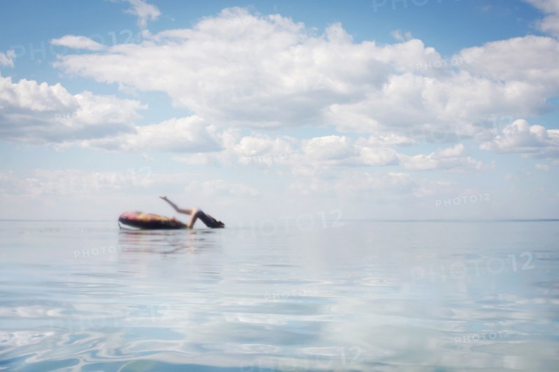 Caucasian teenage girl jumping from inner tube into lake