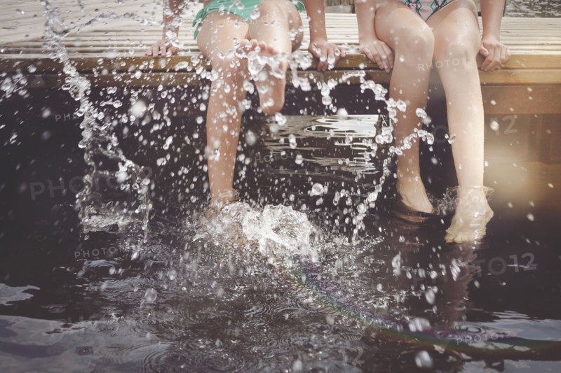 Caucasian girls splashing in lake from wooden dock