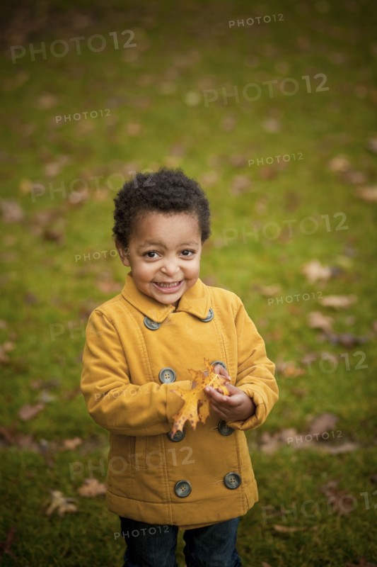 Smiling girl wearing yellow coat holding autumn leaves