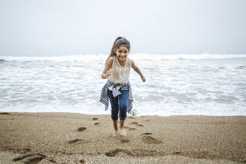 Hispanic girl walking barefoot on beach