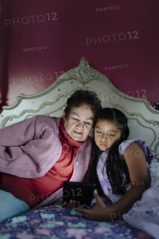 Hispanic grandmother and granddaughter using digital tablet on bed