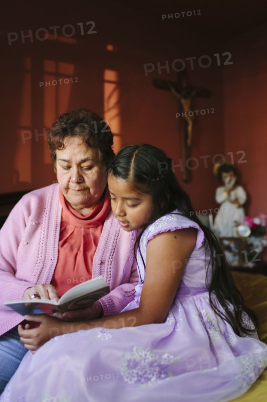 Hispanic grandmother and granddaughter ready book on bed
