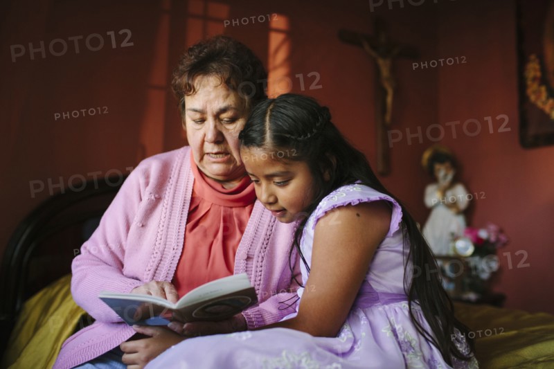 Hispanic grandmother and granddaughter reading book on bed