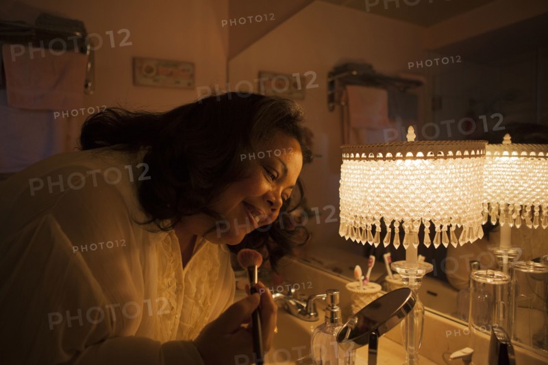 Woman applying makeup in bathroom mirror
