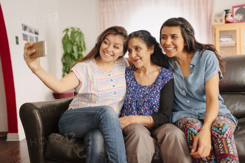 Grandmother and granddaughters taking selfie on sofa