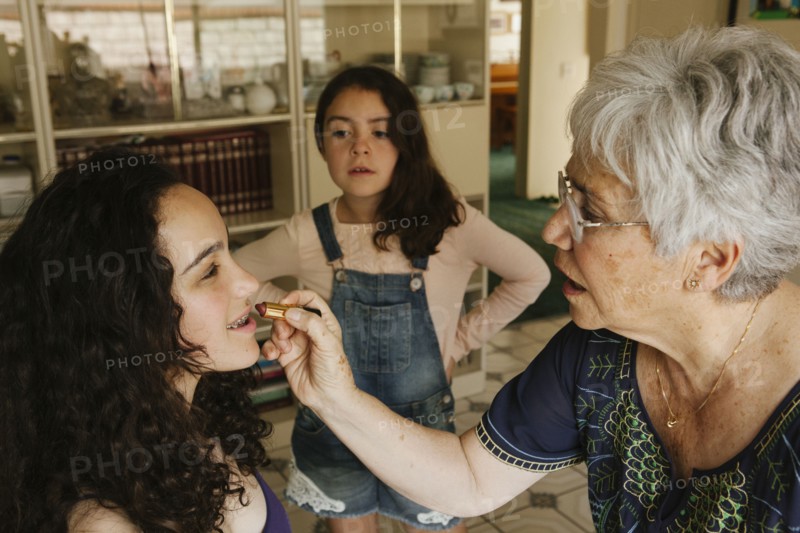 Grandmother applying lipstick to granddaughter in dining room