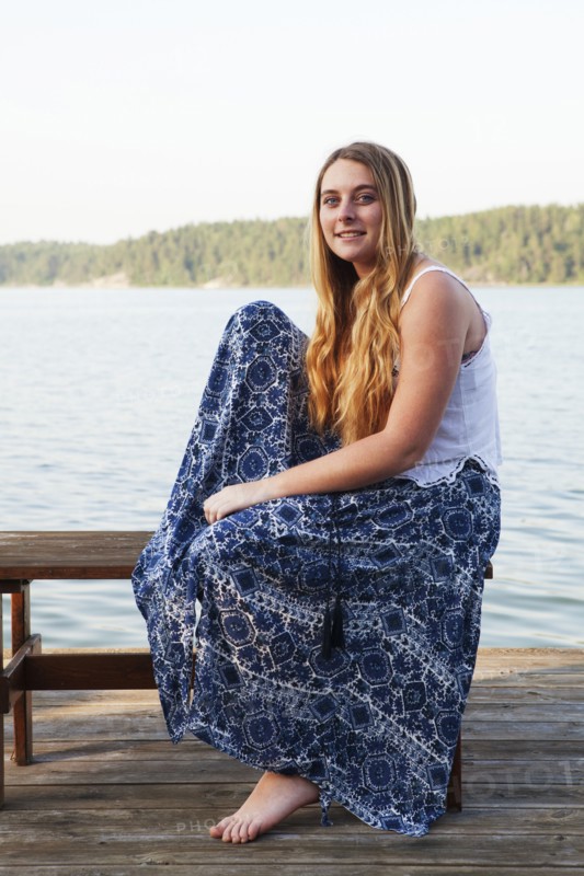 Caucasian teenage girl sitting on wooden dock at lake