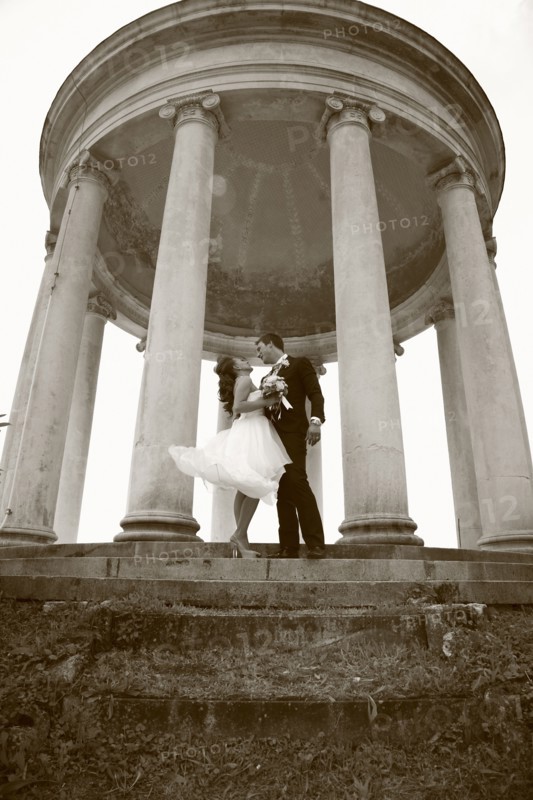 Caucasian bride and groom hugging under columns