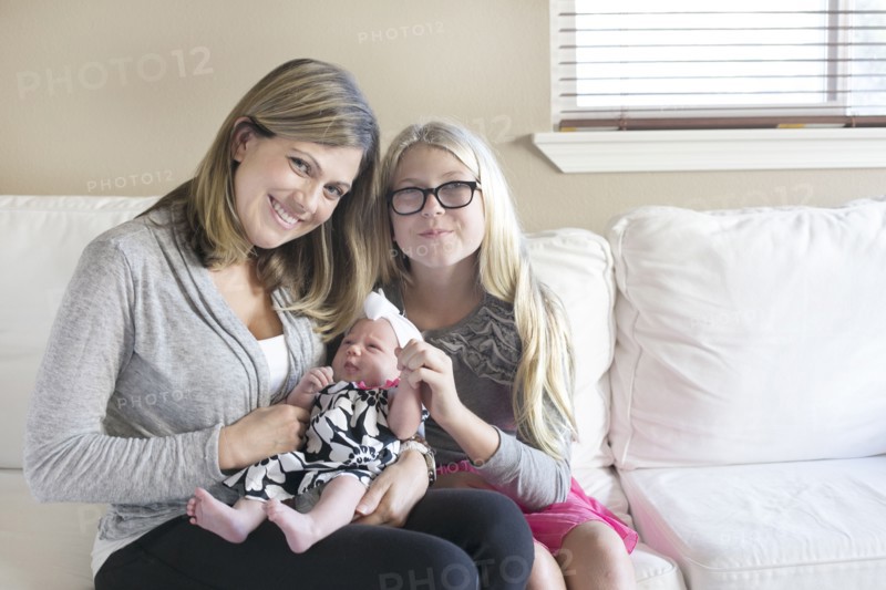 Caucasian mother and daughter cuddling newborn on sofa