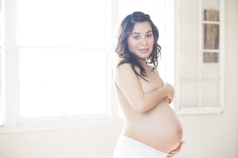 Pregnant nude Hispanic woman holding belly