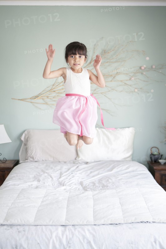 Hispanic girl jumping on bed