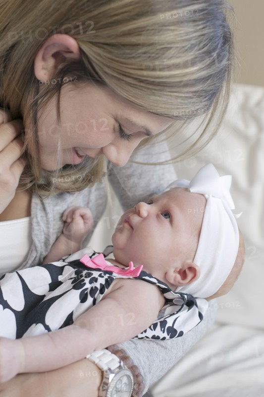 Caucasian mother kissing newborn daughter on sofa