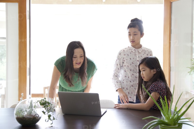 Mother and daughters using laptop in dining room
