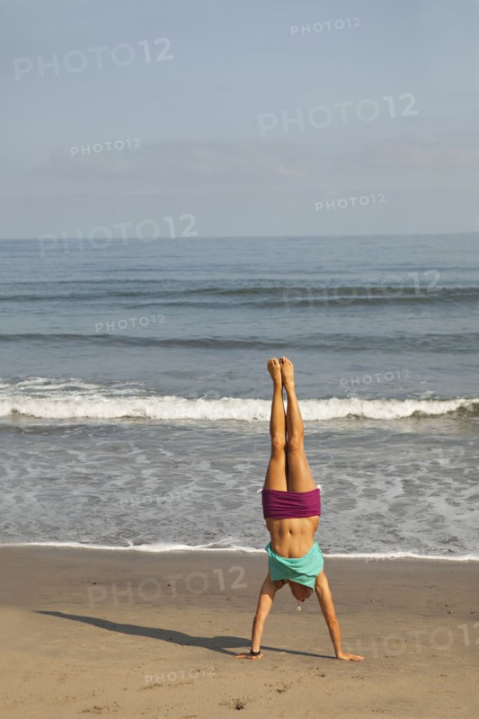 Caucasian woman doing handstand on beach