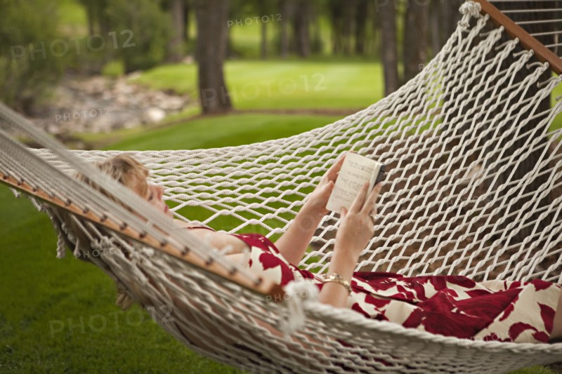 Woman reading book in backyard hammock