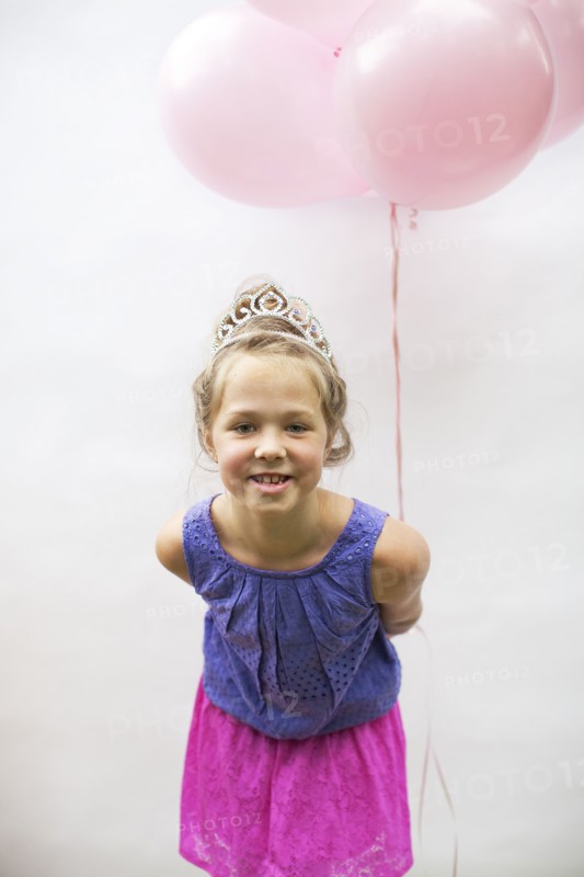 Smiling girl wearing tiara holding pink balloons