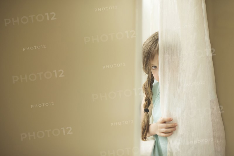 Shy Caucasian girl peeking around curtain