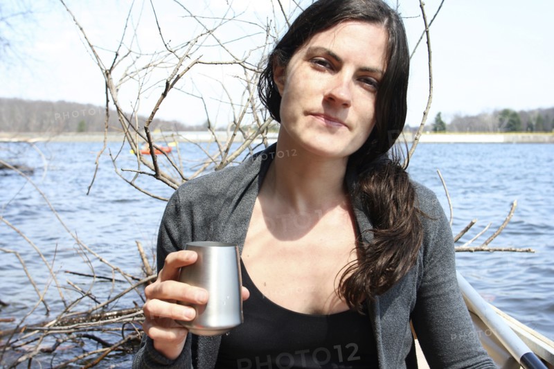 Woman drinking with metal cup in boat on lake