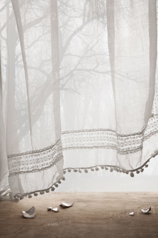 Broken ceramic shards under sheer curtains