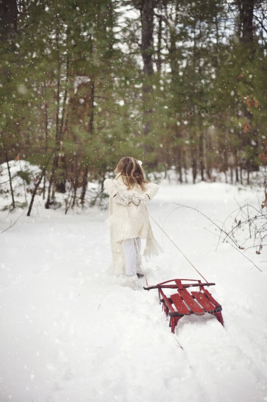 Caucasian girl pulling sled in snowy field