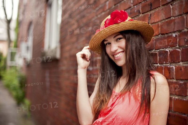Smiling girl wearing straw hat near brick wall