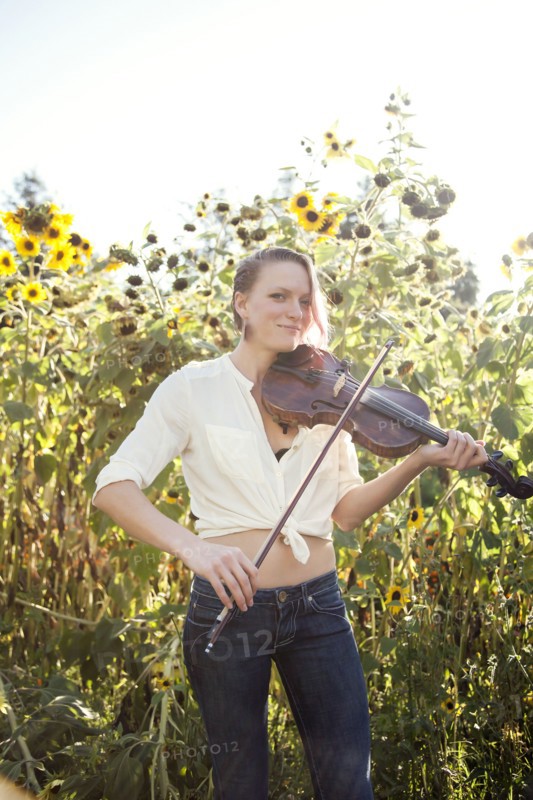 Caucasian musician playing violin in sunflower garden