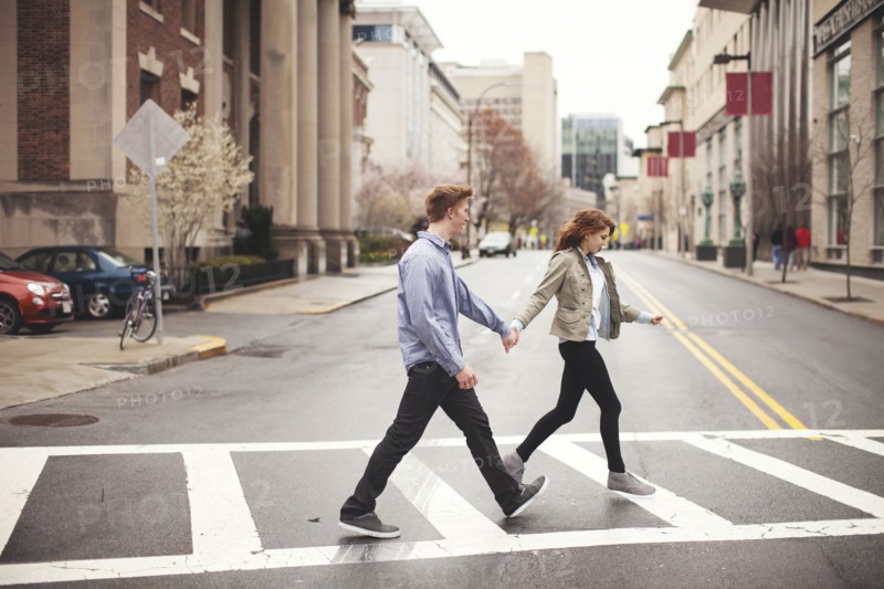 Caucasian couple holding hands crossing city intersection