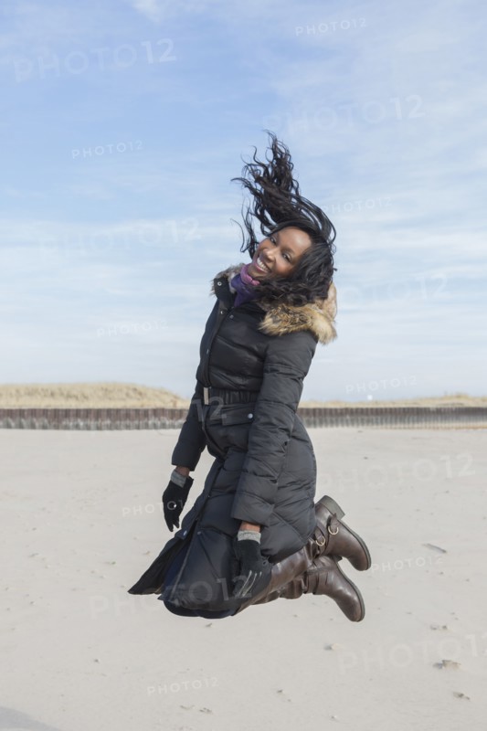 Woman in coat jumping for joy on beach