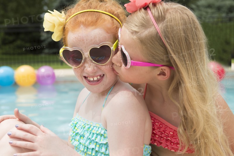 Caucasian girl kissing cheek of friend near swimming pool