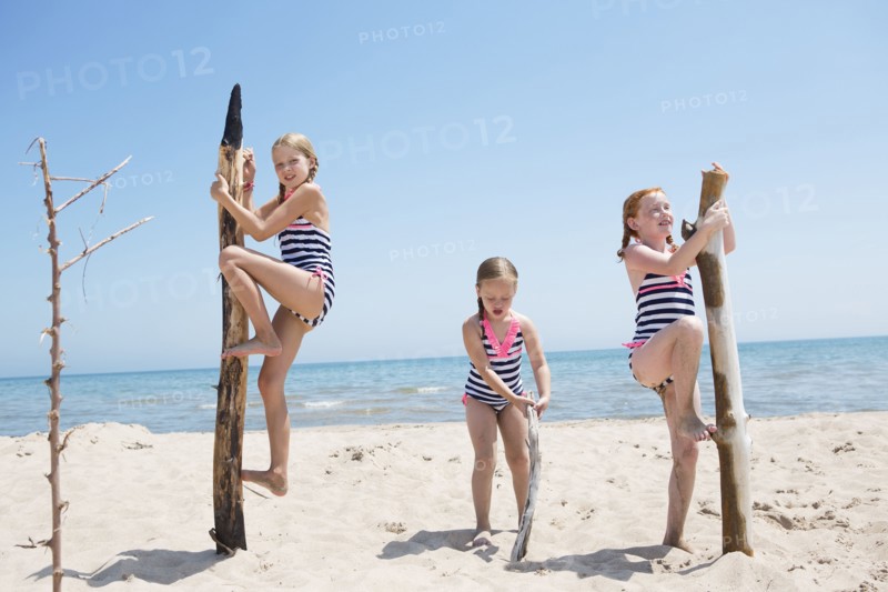 Caucasian girls climbing poles on beach
