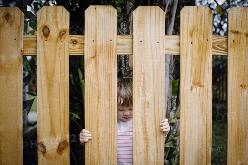 Mixed race girl looking through wooden fence in backyard