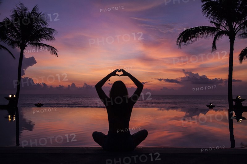 Silhouette of woman gesturing love near swimming pool at sunset