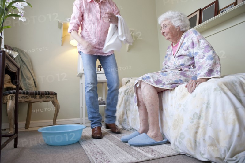Caregiver helping older woman in bedroom