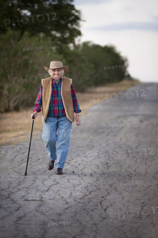 Older Caucasian woman walking with cane on rural road