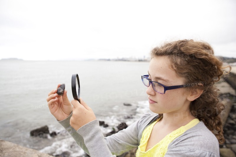 Caucasian girl examining stone with magnifying glass