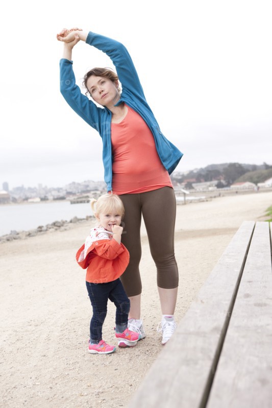Caucasian mother and daughter stretching on beach