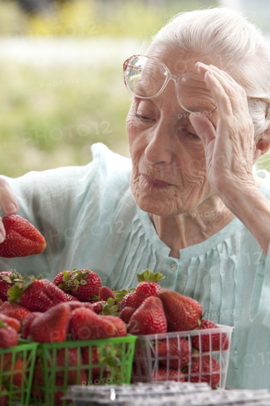 Older Caucasian woman examining strawberries at farmers market