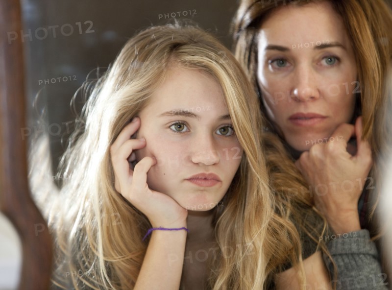 Serious mother and daughter examining themselves in mirror