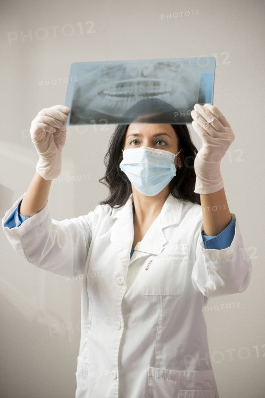 Indian dentist in surgical mask examining x-rays