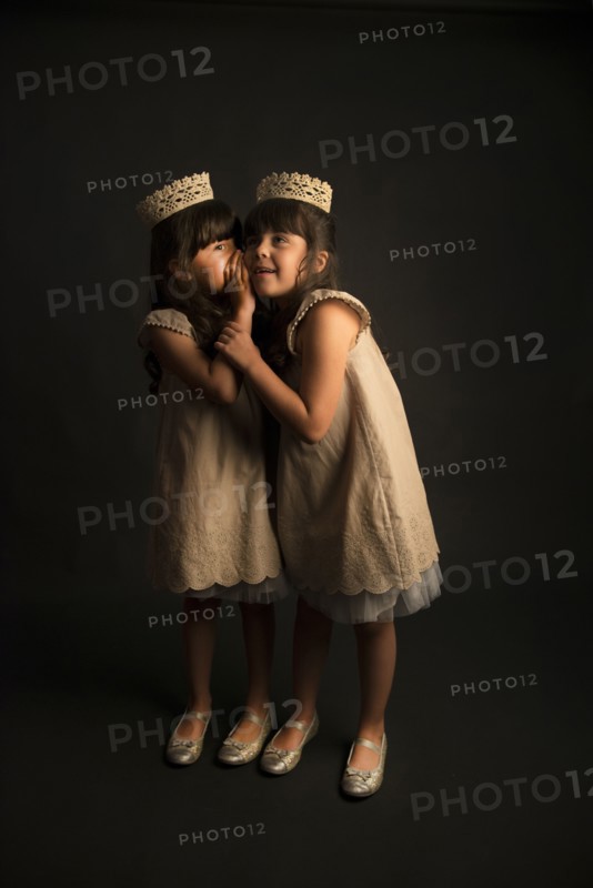Whispering twin girls wearing crowns and princess costumes