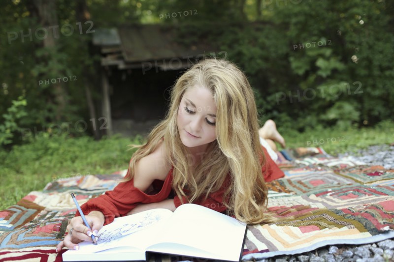 Teenage girl drawing in notebook on blanket