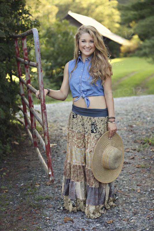 Teenage girl holding straw hat at rural gate